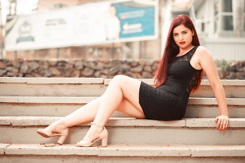 Woman in a Black Dress Sitting on Concrete Steps while Looking at the Camera