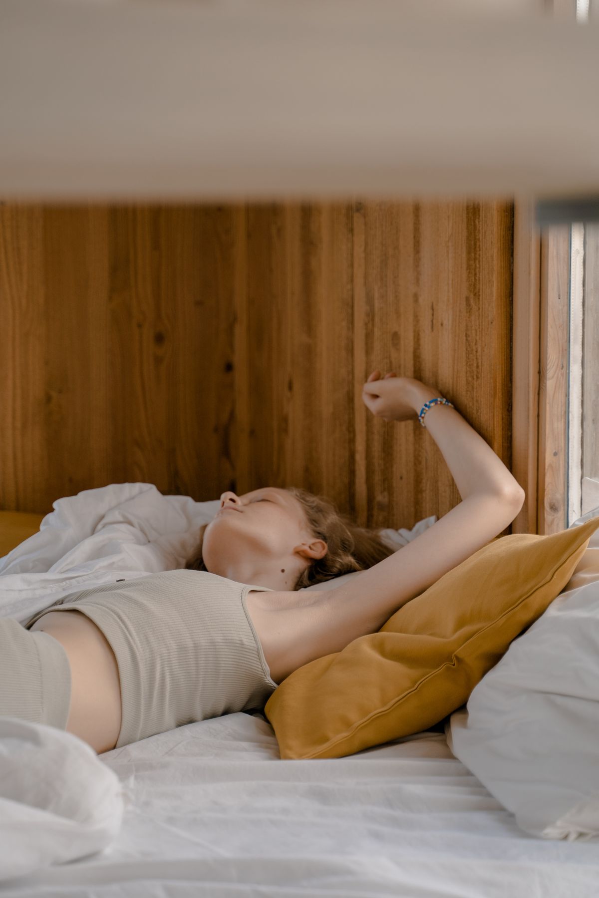 A woman waking and stretching in bed in warm morning light, looking rested.
