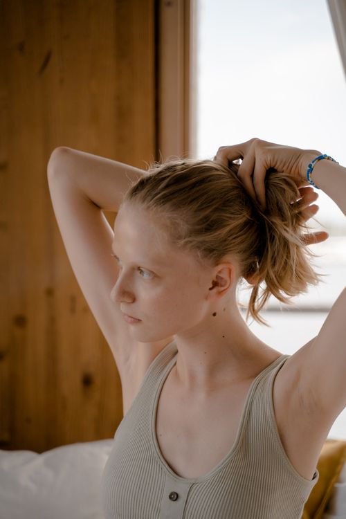 Free A serene image of a woman tying her hair indoors with natural light streaming in. Stock Photo