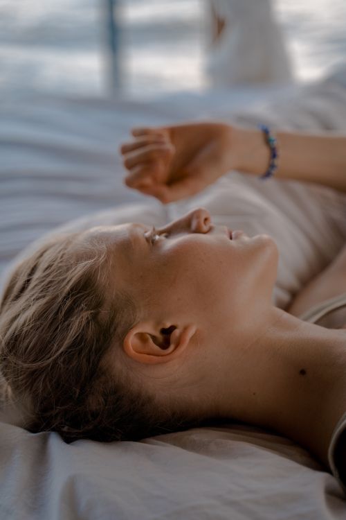 Free A serene woman lies in bed, enjoying a moment of relaxation on a sunny day. Stock Photo