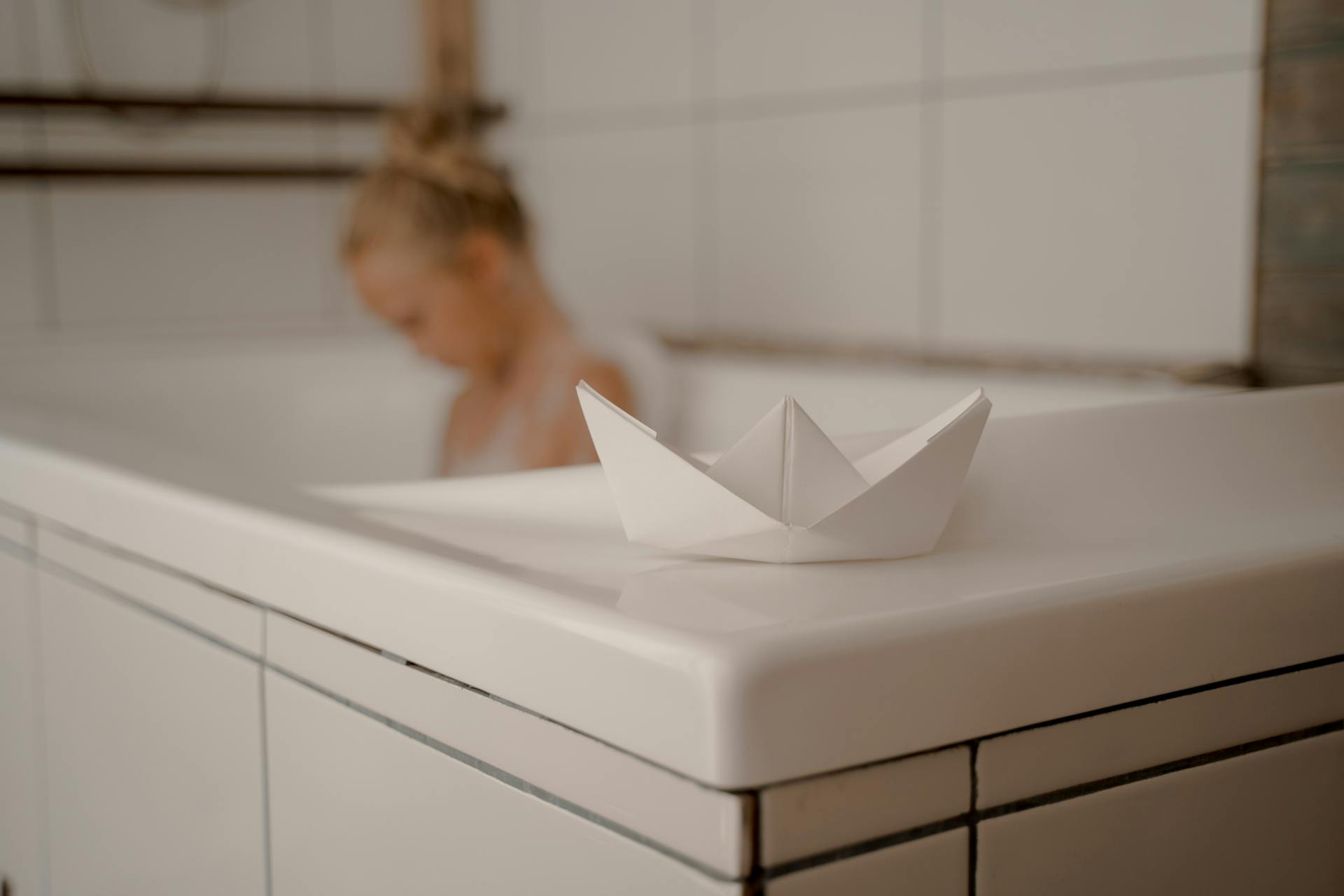 Paper Boat on Bathtub with Child during Bubble Bath in Background
