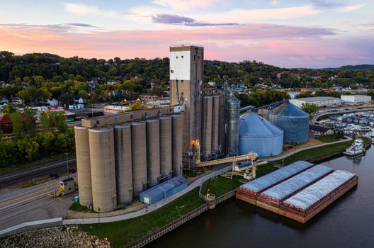 Aerial view of grain silos by a river in Red Wing, MN at sunset, showcasing industrial landscape.