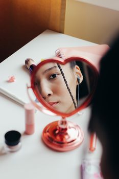 Close-up of a woman's face in a heart-shaped mirror with makeup items.