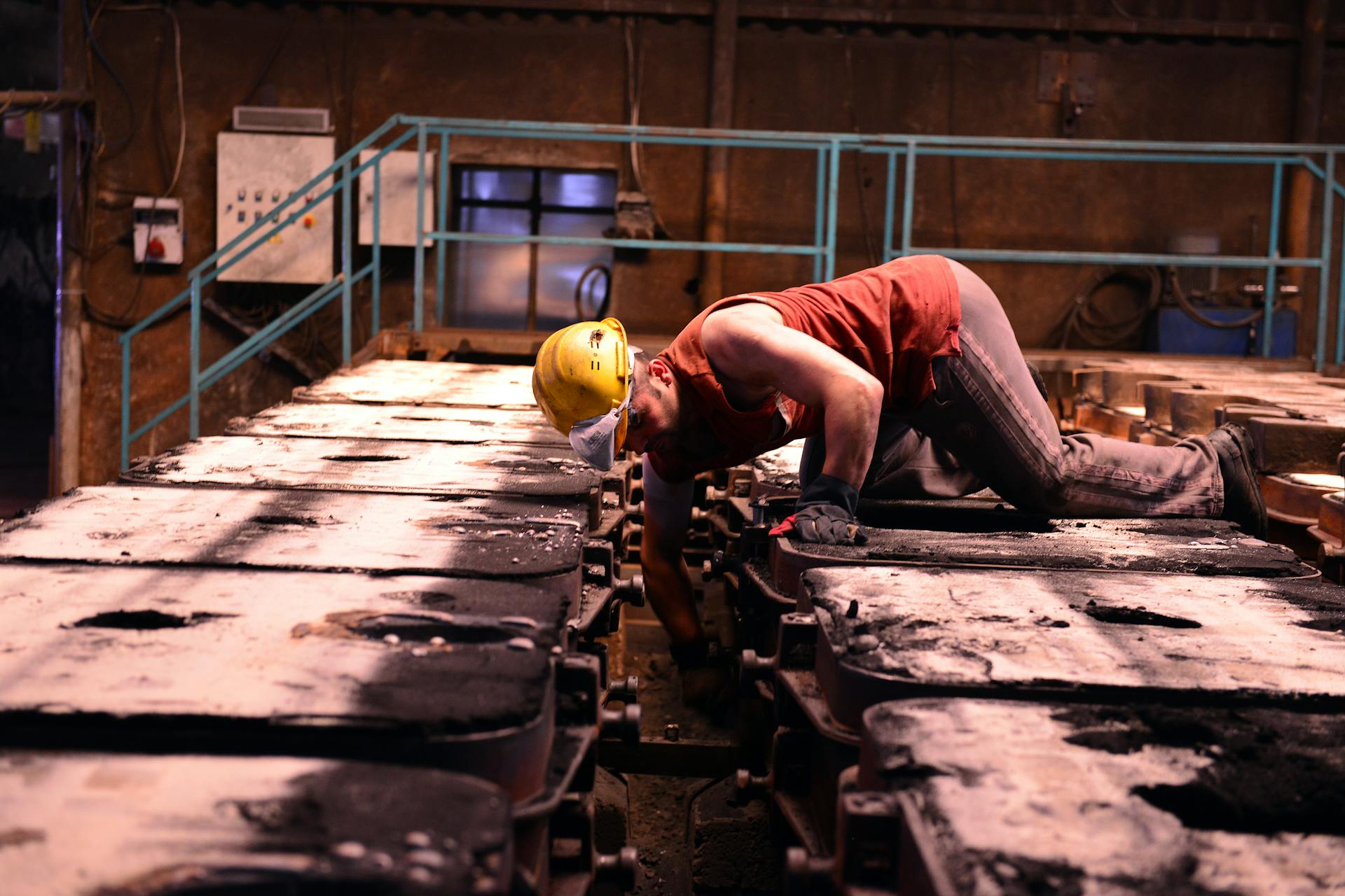 Worker inspecting machinery in an industrial plant wearing safety gear.