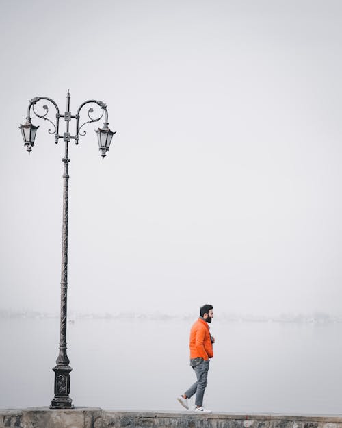 Man in an Orange Jacket Walking Near a Street Lamp
