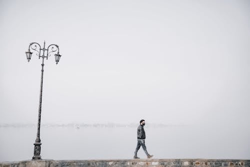 Photo of a Man in a Black Jacket Walking Near a Street Lamp