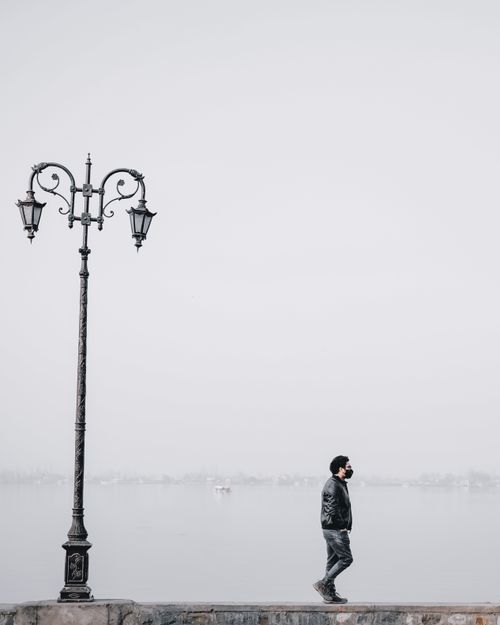 Free A solitary man walks along a waterfront on a foggy day, emphasizing solitude and tranquility. Stock Photo