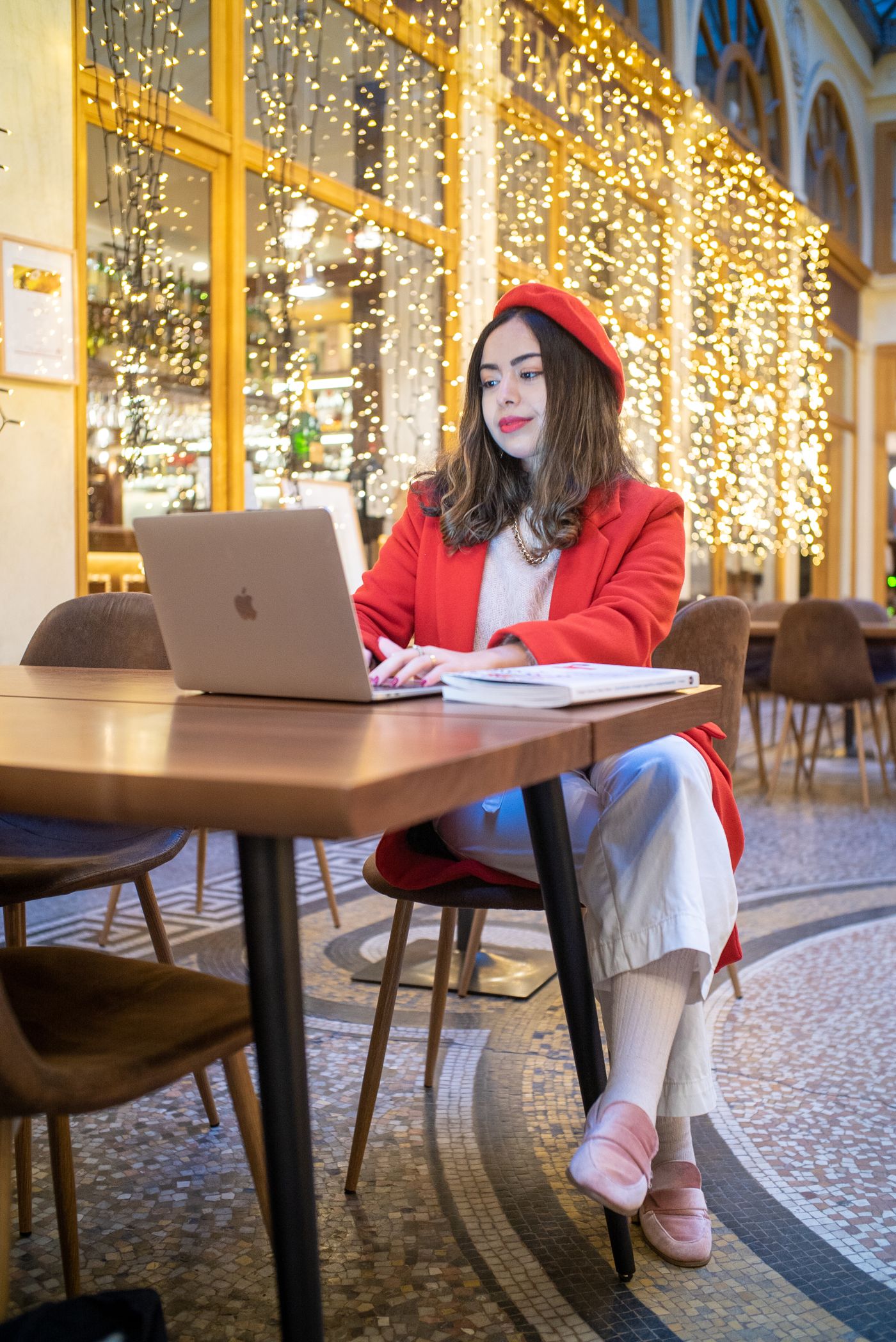 Jeune femme en manteau rouge qui travaille sur un ordinateur portable dans un café parisien