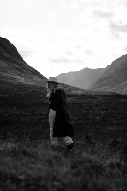 Grayscale Photo of Woman in Black Coat Standing on Grass Field