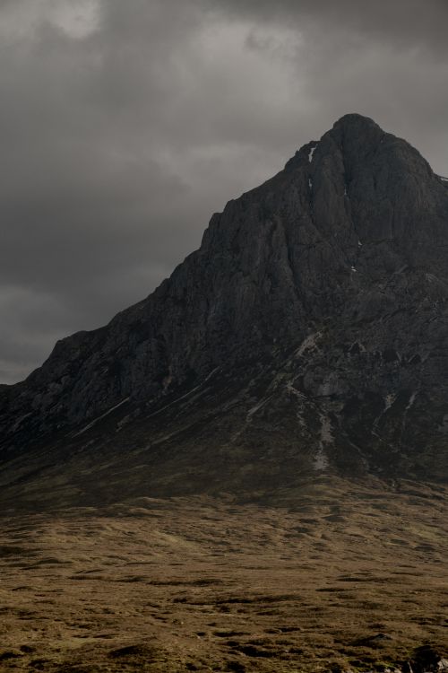 Free A towering mountain peak set against a cloudy, dramatic sky, evoking a sense of isolation and grandeur. Stock Photo