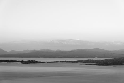 A peaceful monochrome landscape of mountains and coastlines in misty weather.
