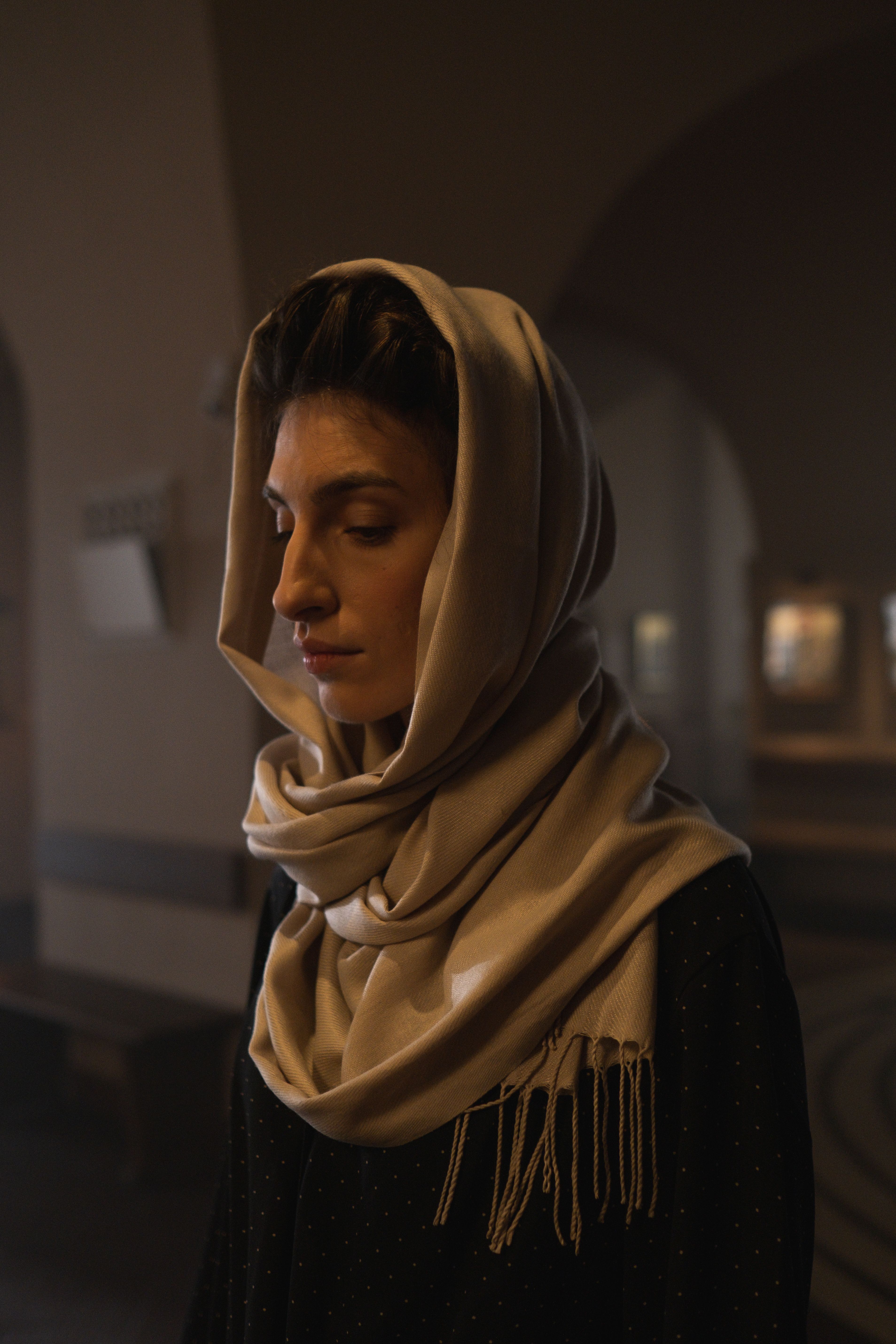 A contemplative woman wearing a scarf indoors, embodying reflection and tranquility.