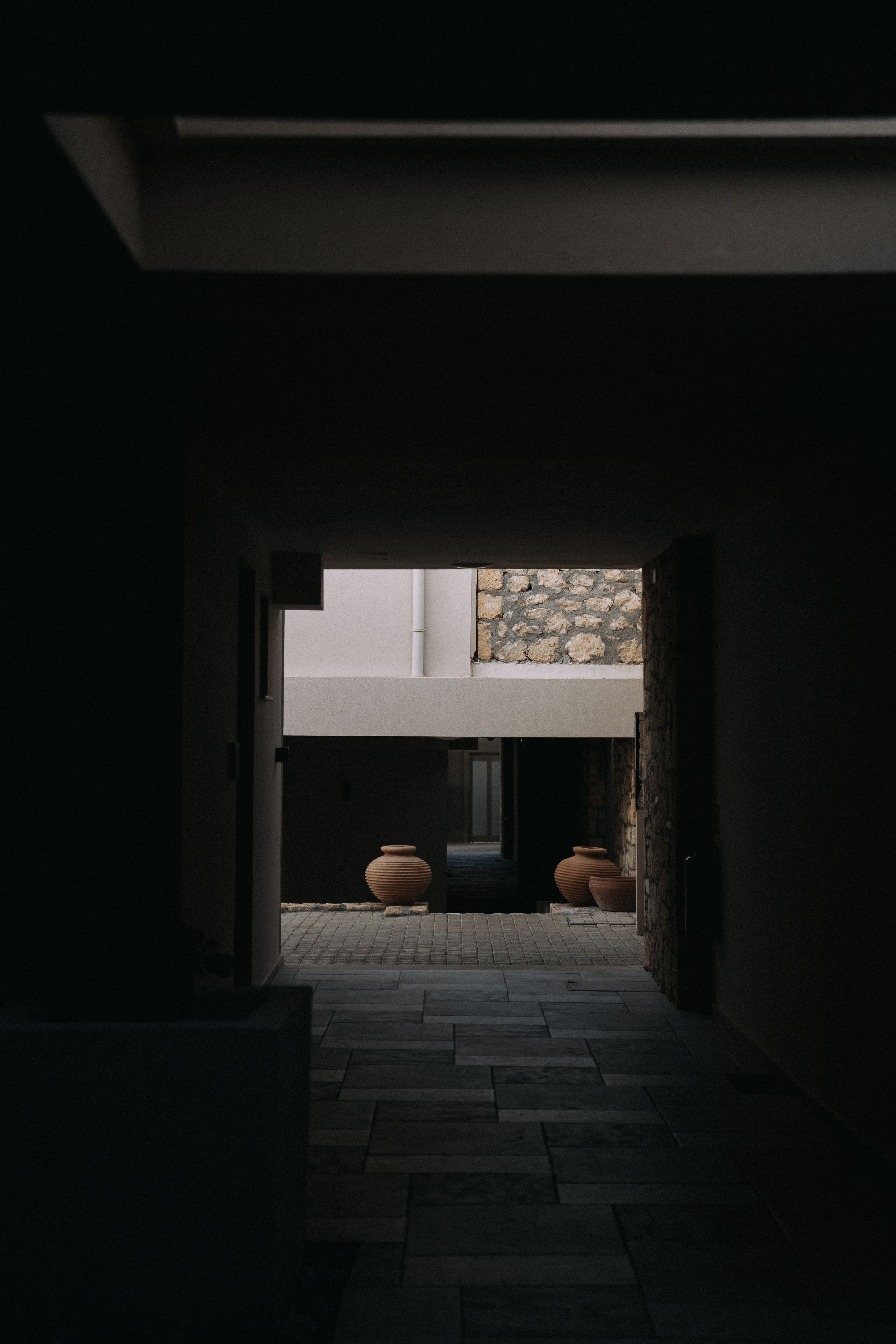 A mysterious tunnel leads to an outdoor area with stone walls and terracotta vases.