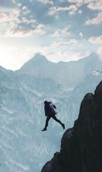 Man jumping across a rocky chasm with a breathtaking mountain range in the background.