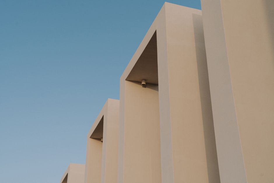 Minimalist beige building facade against a blue sky, showcasing modern architectural design.