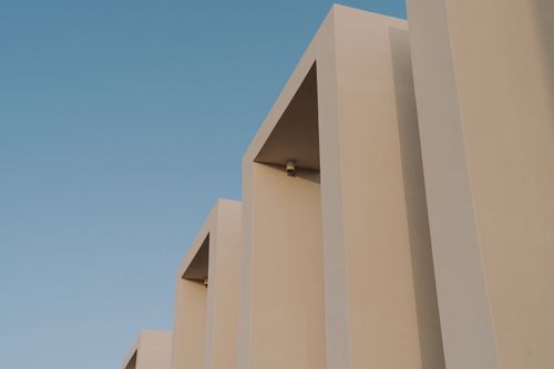Free Minimalist beige building facade against a blue sky, showcasing modern architectural design. Stock Photo