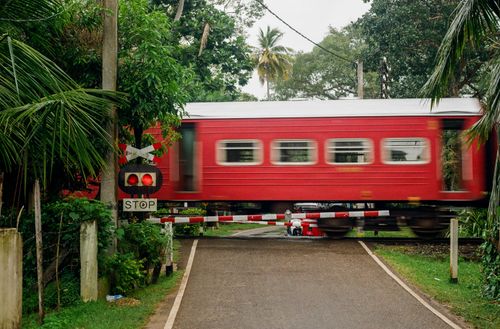 Free Red train swiftly crosses tropical rural railway stop with blurred motion. Stock Photo