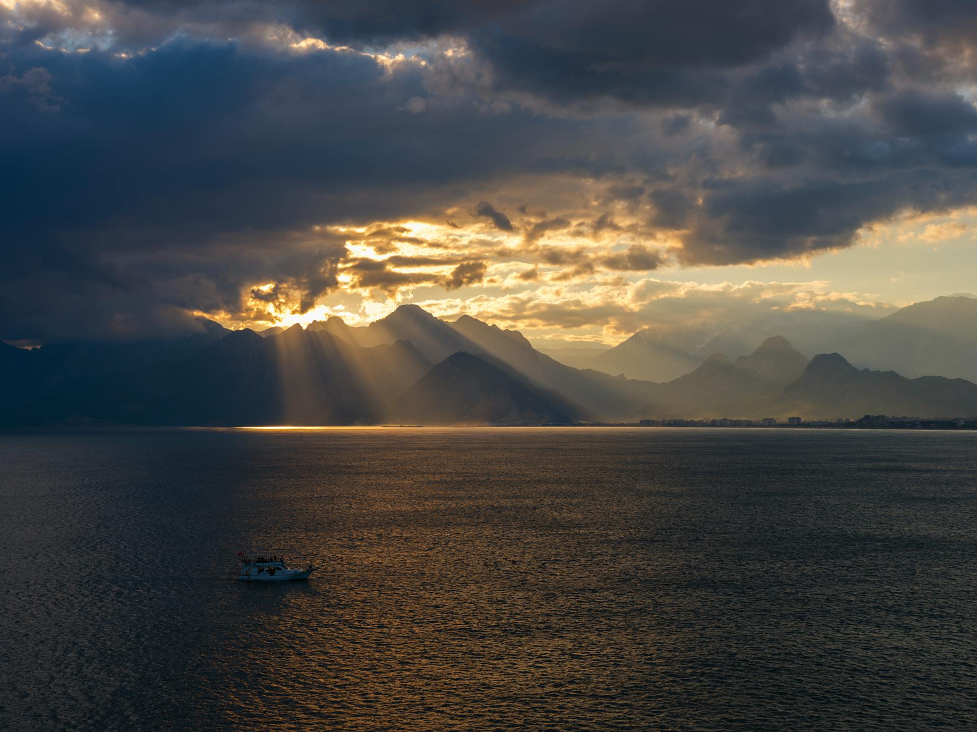 Tranquil sunrise with sun rays piercing clouds over mountains reflected on the sea.