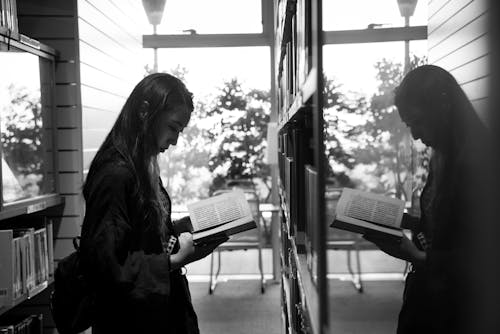 ガラスに映る本を読んでいる女の子のグレースケール写真