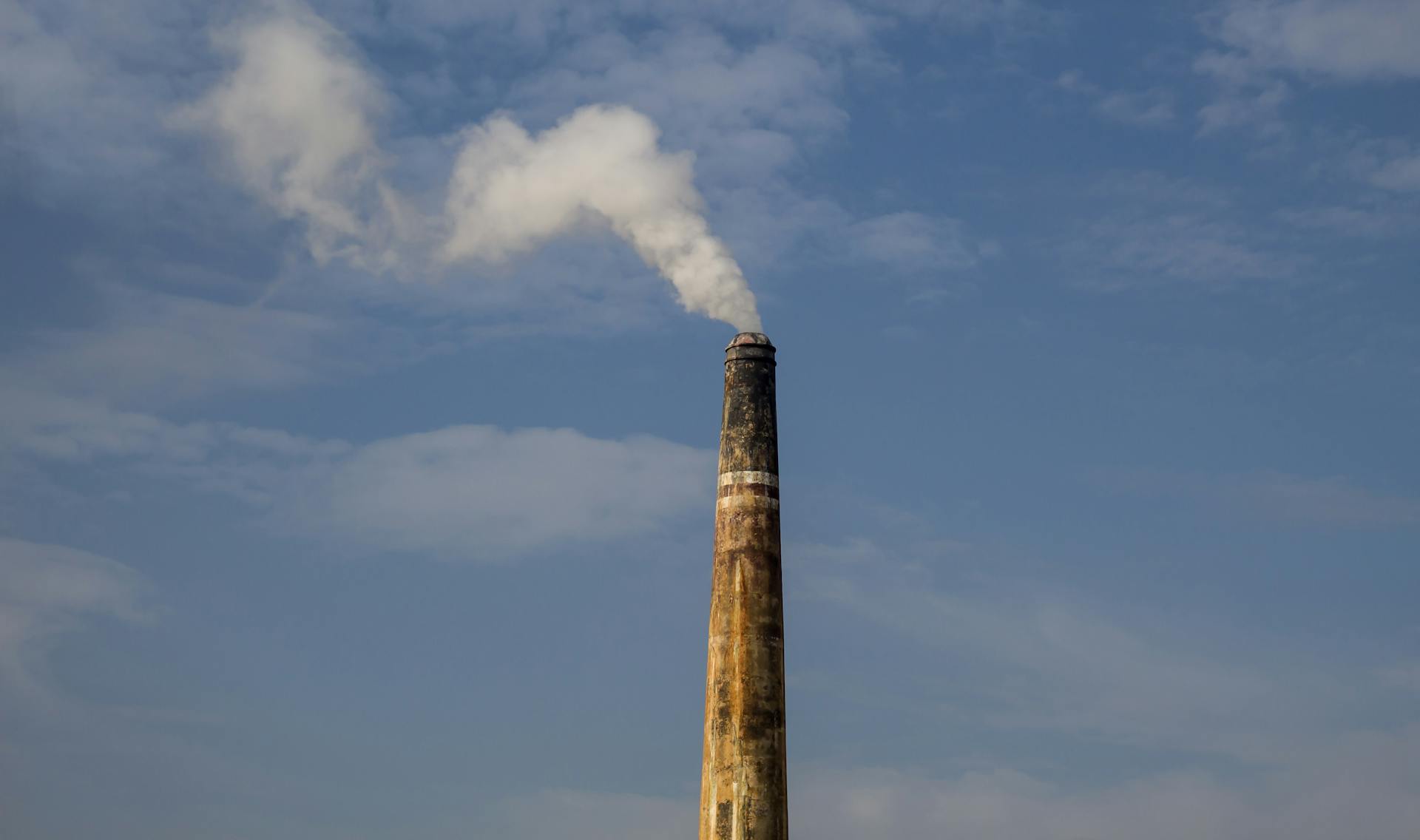 A factory chimney releasing smoke against a clear blue sky, highlighting air pollution.