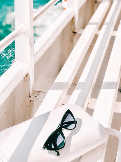 Free Black Sunglasses Laying on White Bench of Cruise Ship Stock Photo