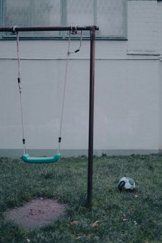 A tranquil playground scene with an empty swing next to a soccer ball on grass.