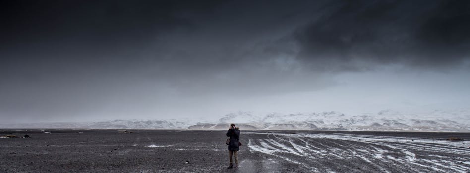 A lone photographer in a vast, desolate mountain landscape under dramatic skies.