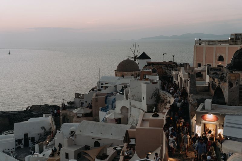 Explore the stunning sunset view over Oia, Santorini with iconic windmills and serene Aegean Sea.