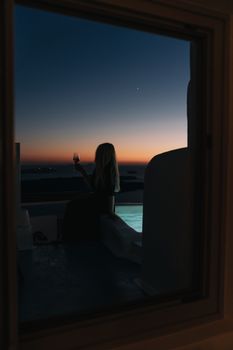 Woman on balcony with wine glass during sunset, offering a tranquil resort view.