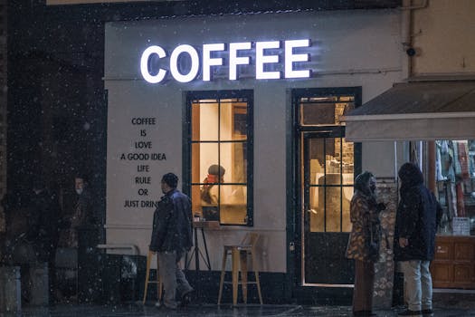 Warm light glows from a coffee shop window as snow falls, capturing a chilly night scene in Konya, Turkey.