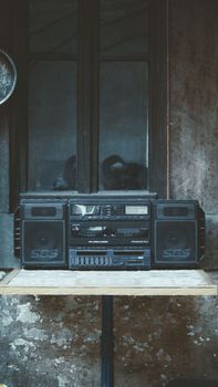 An old-fashioned SBS brand boombox on a rustic table against a weathered wall.