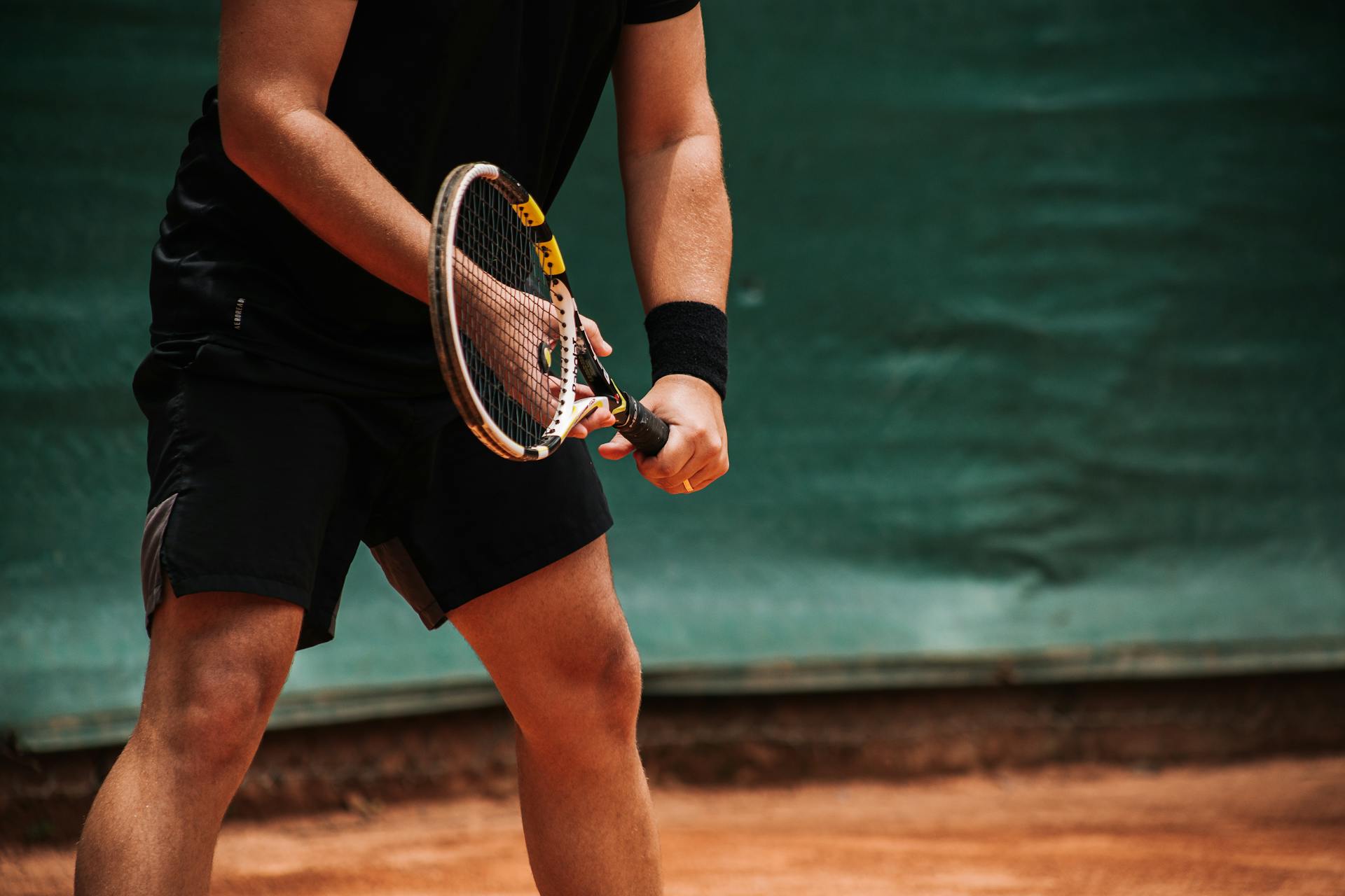 Close-up of a tennis player holding a racket, ready to serve on an outdoor clay court.