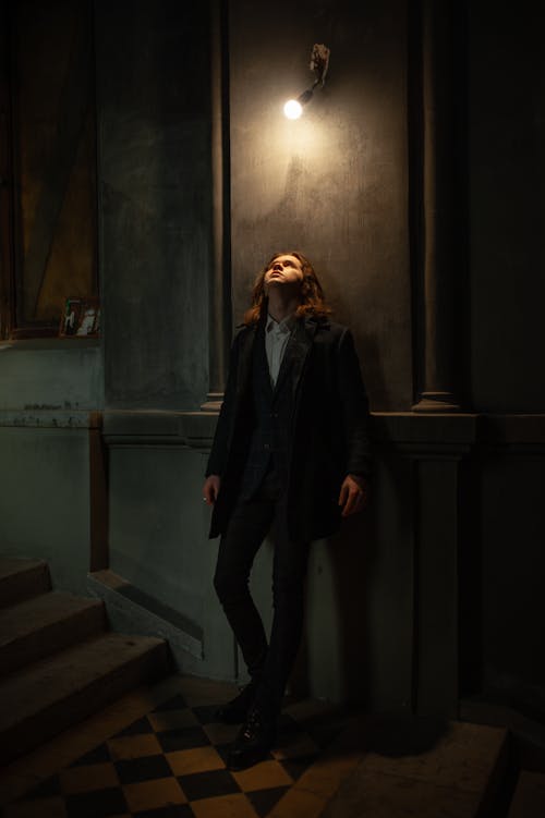 Long Haired Man Standing under Wall Lamp