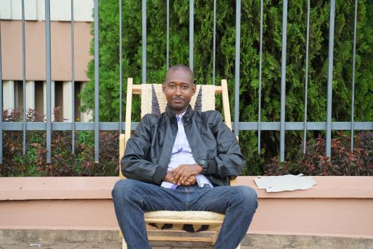 Man in leather jacket sitting on chair outdoors in Kigali, Rwanda.