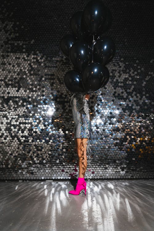A Model in a Glittery Outfit Holding Black Balloons