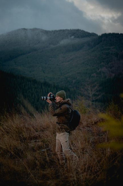 Man photographing mountains in autumn, showcasing outdoor adventure and travel.