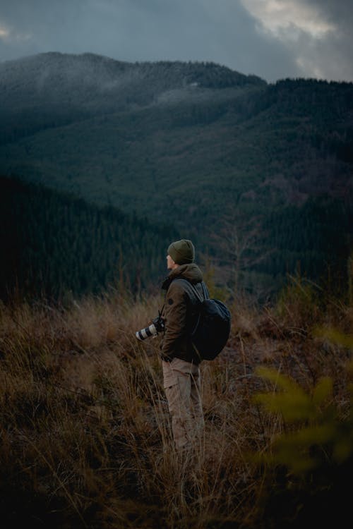 Man in Jacket with Camera Standing Against Mountain