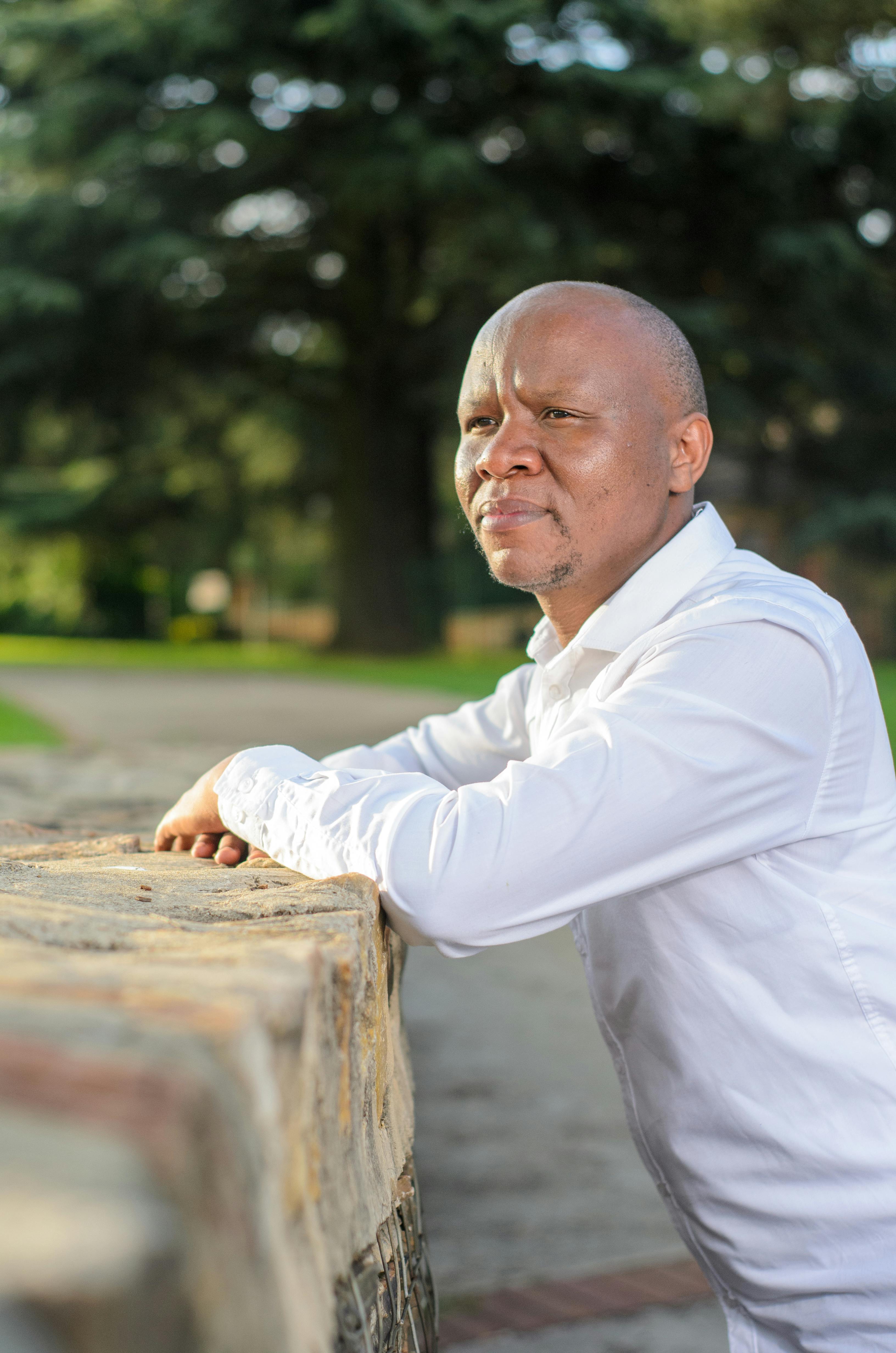 Portrait of an African American man leaning on a stone wall outdoors wearing a white shirt.