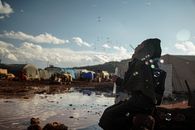 Hijabi Woman Kneeling by Puddle in Refugee Camp Blowing Bubbles