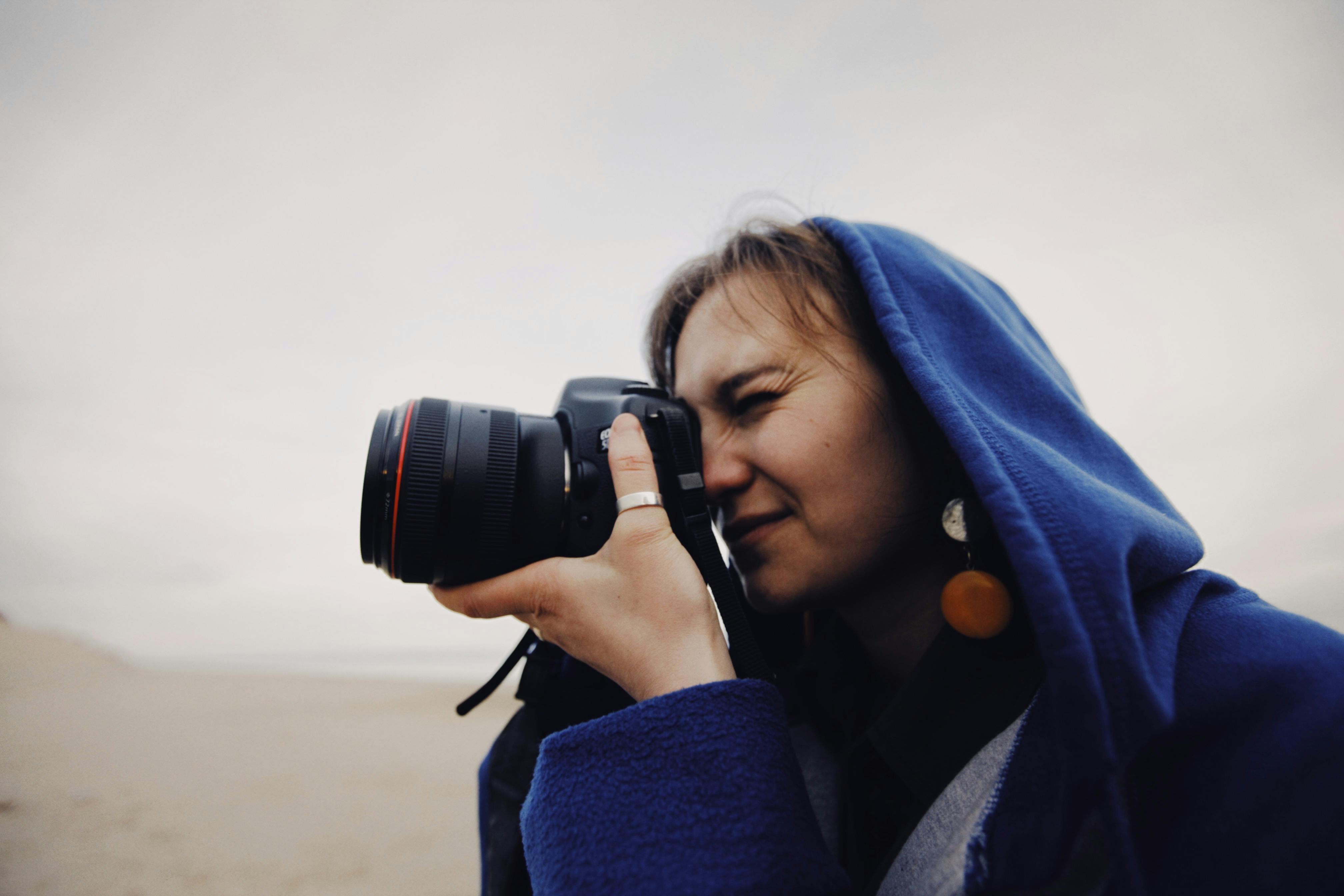 Free A person in a blue hoodie takes photos with a black camera on a beach. Stock Photo