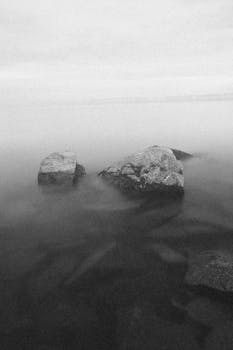 Serene black and white photo of ocean rocks with calm water.
