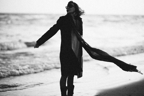 Free Black and white image of a woman standing on a beach, embracing the ocean breeze. Stock Photo
