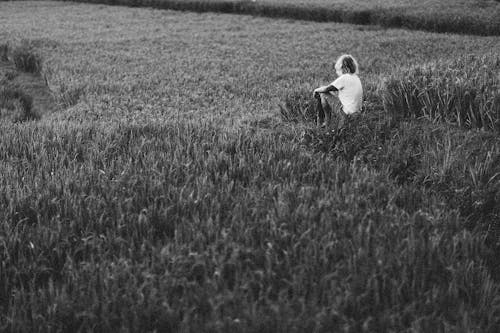 Grayscale Photo of Woman in White Shirt Sitting on Cropland