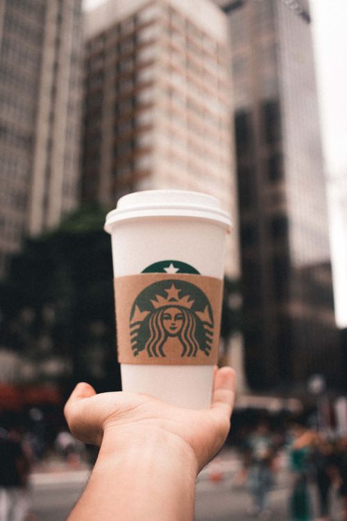 Free A hand holding a coffee cup in an urban setting, showcasing a vibrant city life. Stock Photo
