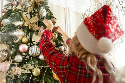 
A Woman Wearing a Christmas Hat Decorating a Christmas Tree