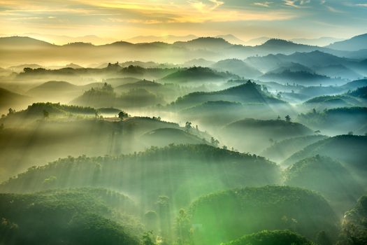 A breathtaking aerial landscape with sunrays piercing through misty hills at sunrise.
