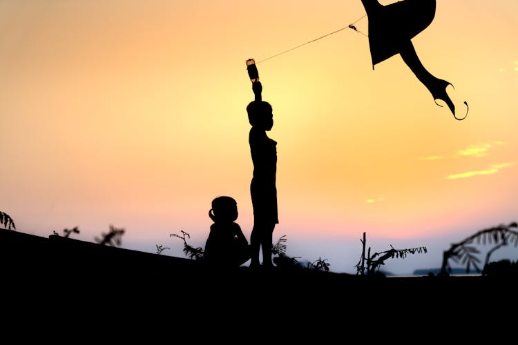 Silhouette Of A Kid Playing With A Kite