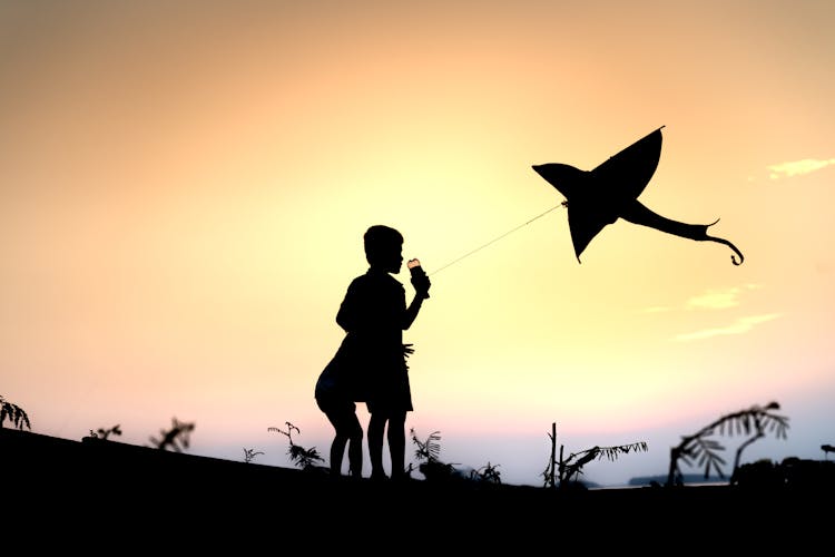 Silhouette Of Children Playing With A Kite