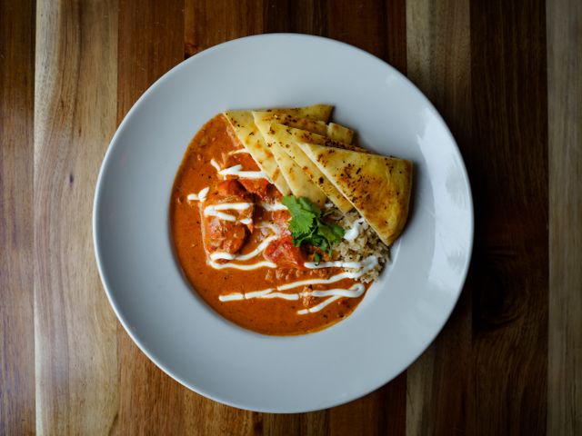 Top view of a flavorful butter chicken dish served with naan and garnished with cilantro.