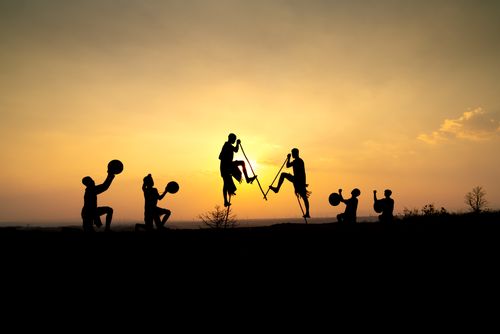 Free Group of people silhouetted against a sunset, performing with drums and stilts. Stock Photo